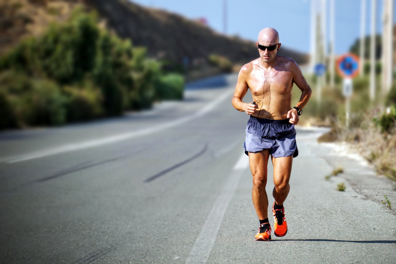 Bald man with sunglasses, hit and sweaty running along a road on a hot day.